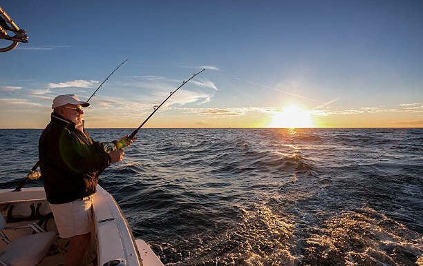 Man fishing on the ocean from the back of his boat at sunset